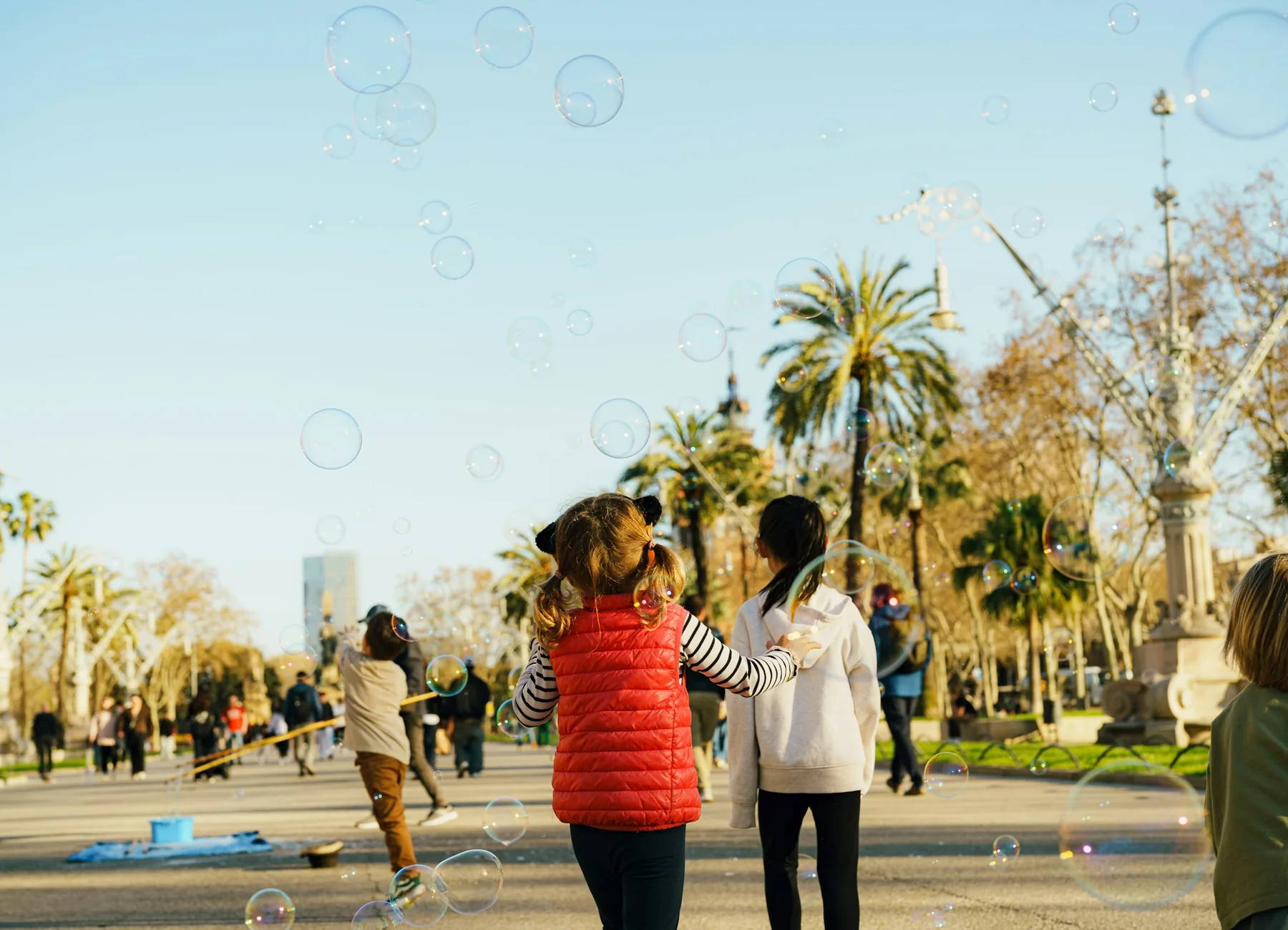 Niñas y niños jugando con pompas de jabón entre palmeras en Barcelona